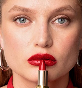 A woman applying red lipstick to lips